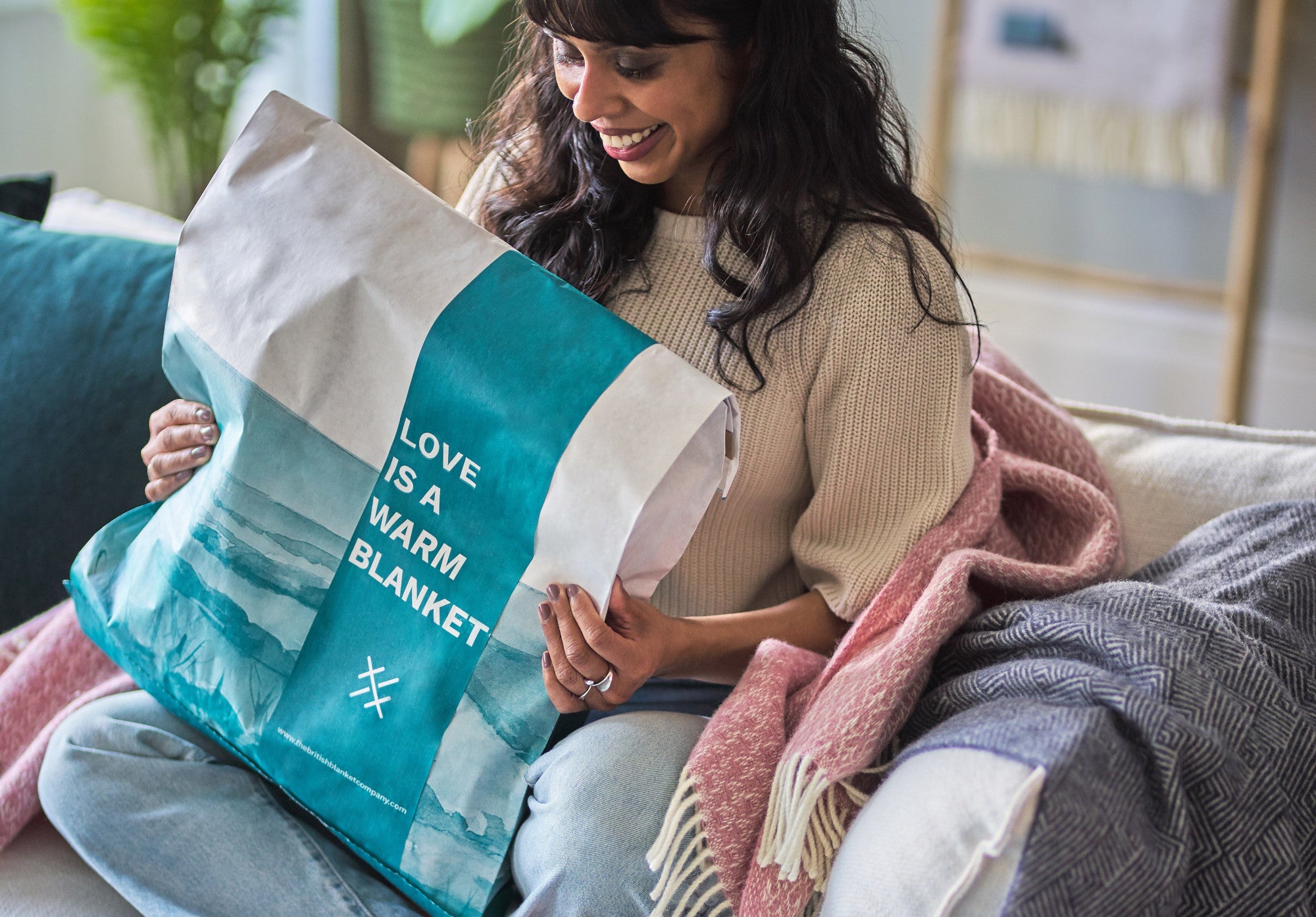 A woman sitting on a couch, smiling, and holding a bag, representing comfort and fashion in an indoor setting.