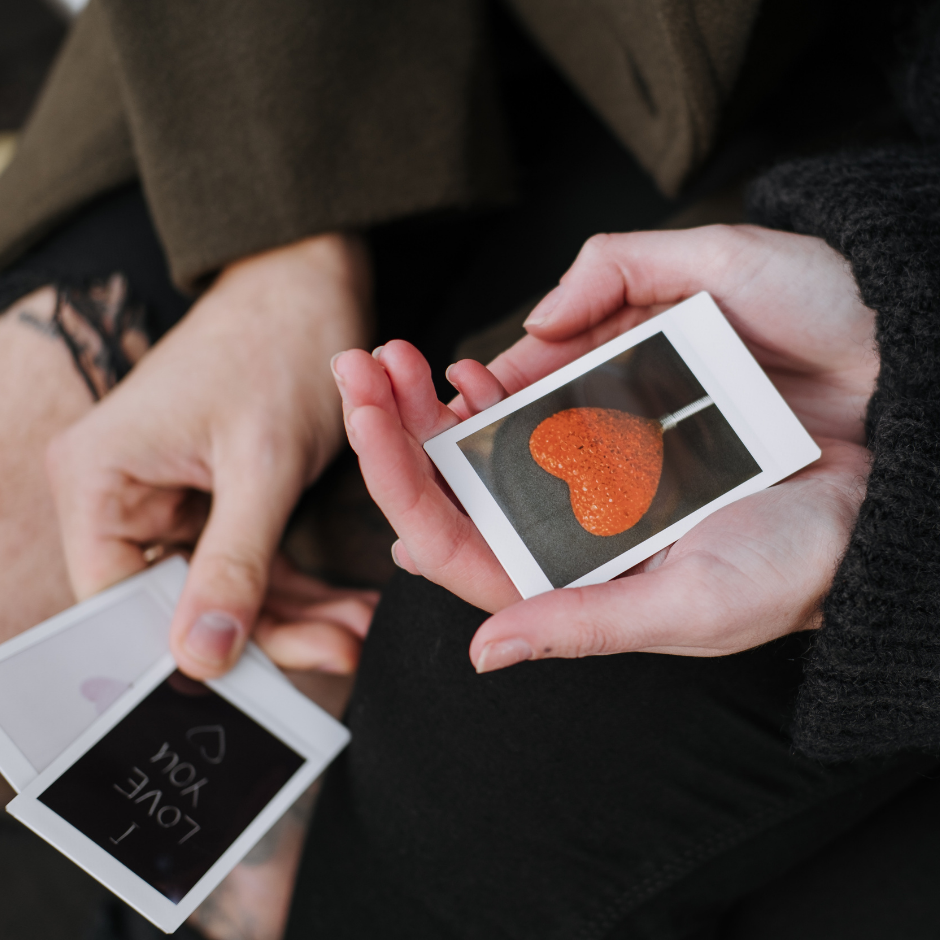 A person holds a mobile phone displaying a photo of a heart, with a close-up focus on their hand.