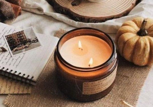 A candle in a jar on a table, accompanied by a close-up of a pumpkin, creating a cozy, autumnal still life scene.