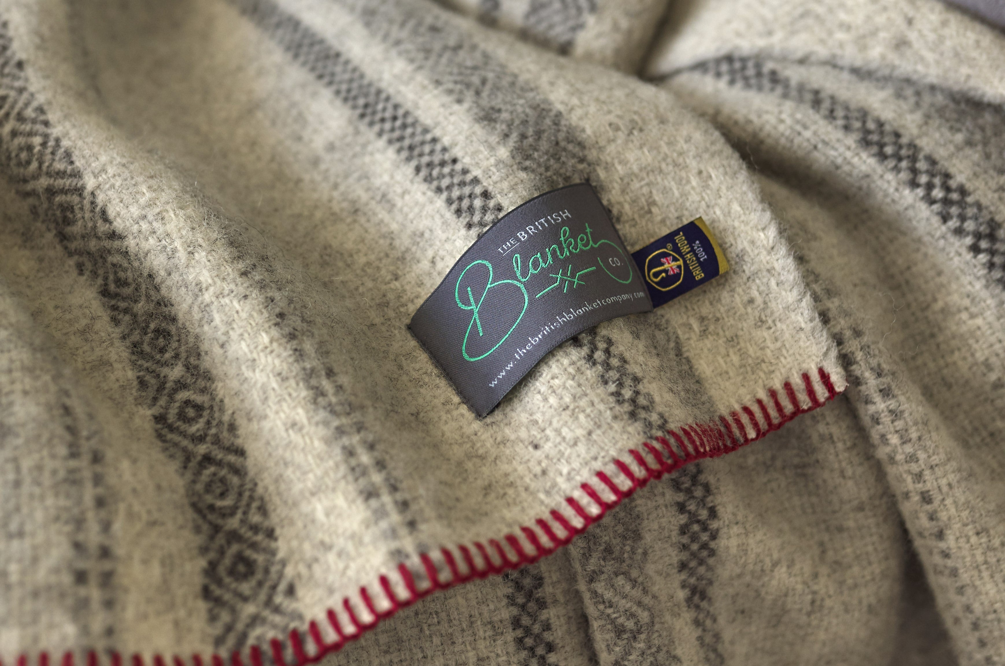 Close-up of a blanket featuring a stitched label with a heart and letter design on textured fabric.