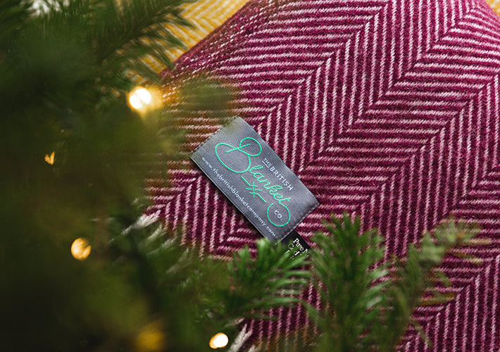 A blanket with a tag features a Christmas tree design, showcasing green hues and festive ornament details.