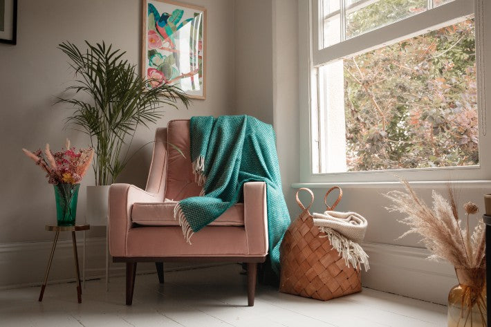 Modern lounge corner with teal blanket draped over a pink armchair