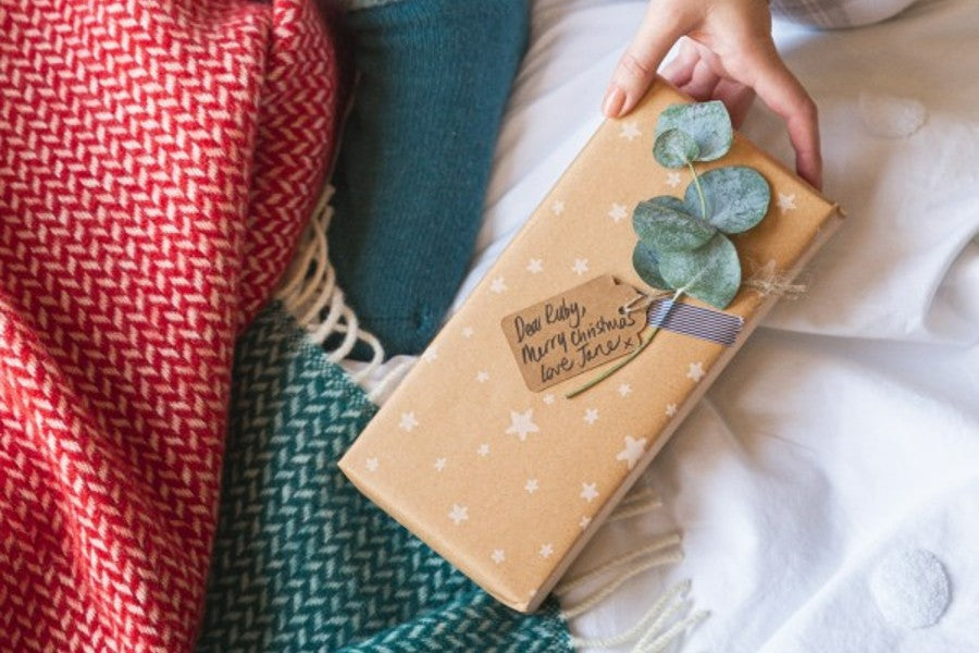 Hand holding a wrapped Christmas gift over a blanket-strewn bed