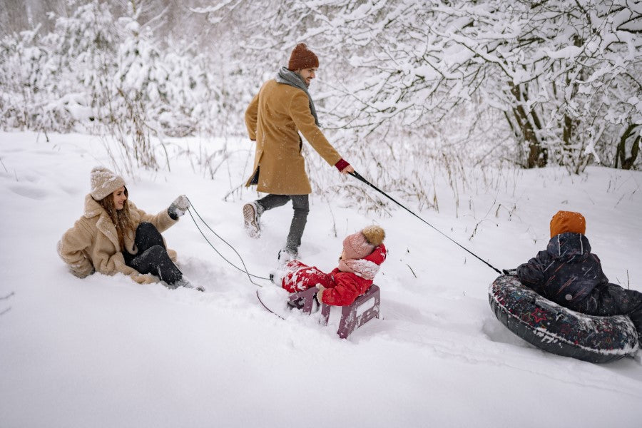 A group of people enjoying sledding in the snow, including a child in a snow tube and a baby in a sled.