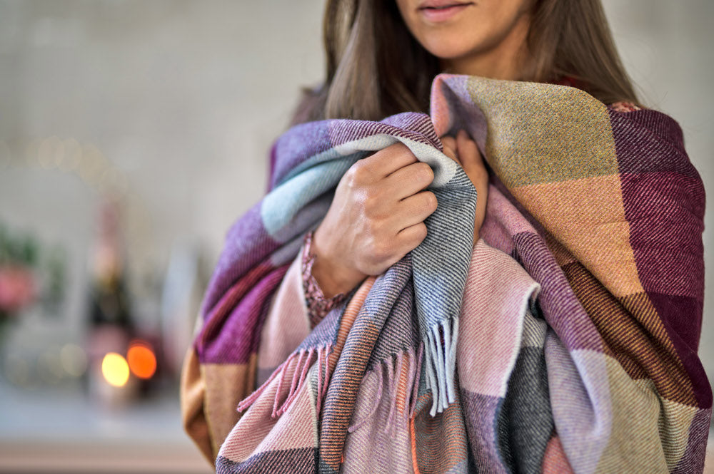 A woman holds a colorful shawl, showcasing its intricate patterns, with a focus on her face and hand gripping the fabric.