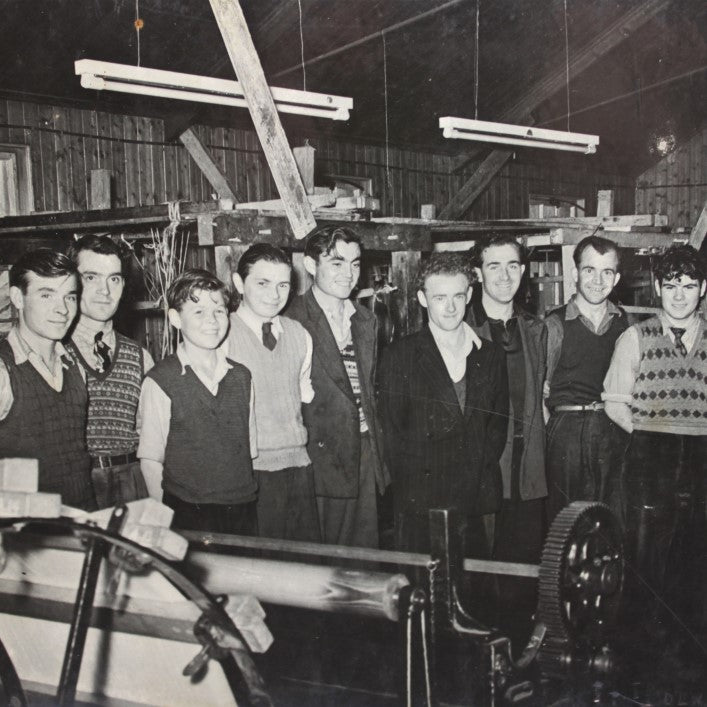 A group of people, including men in suits and vests, posing for a photo in a black and white indoor setting.