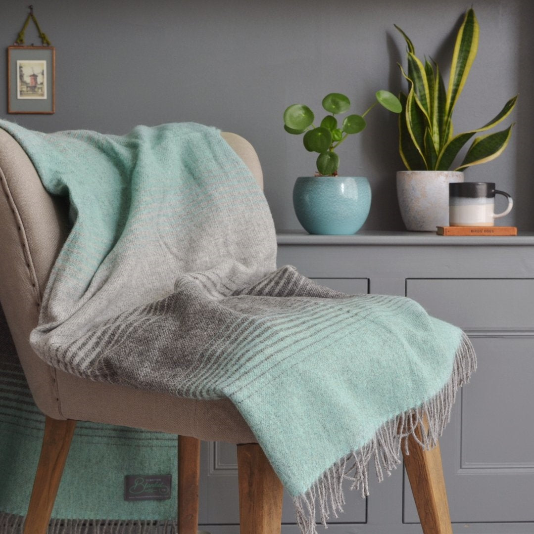 A cozy chair draped with a blanket, surrounded by potted plants, and a mug on a nearby surface.