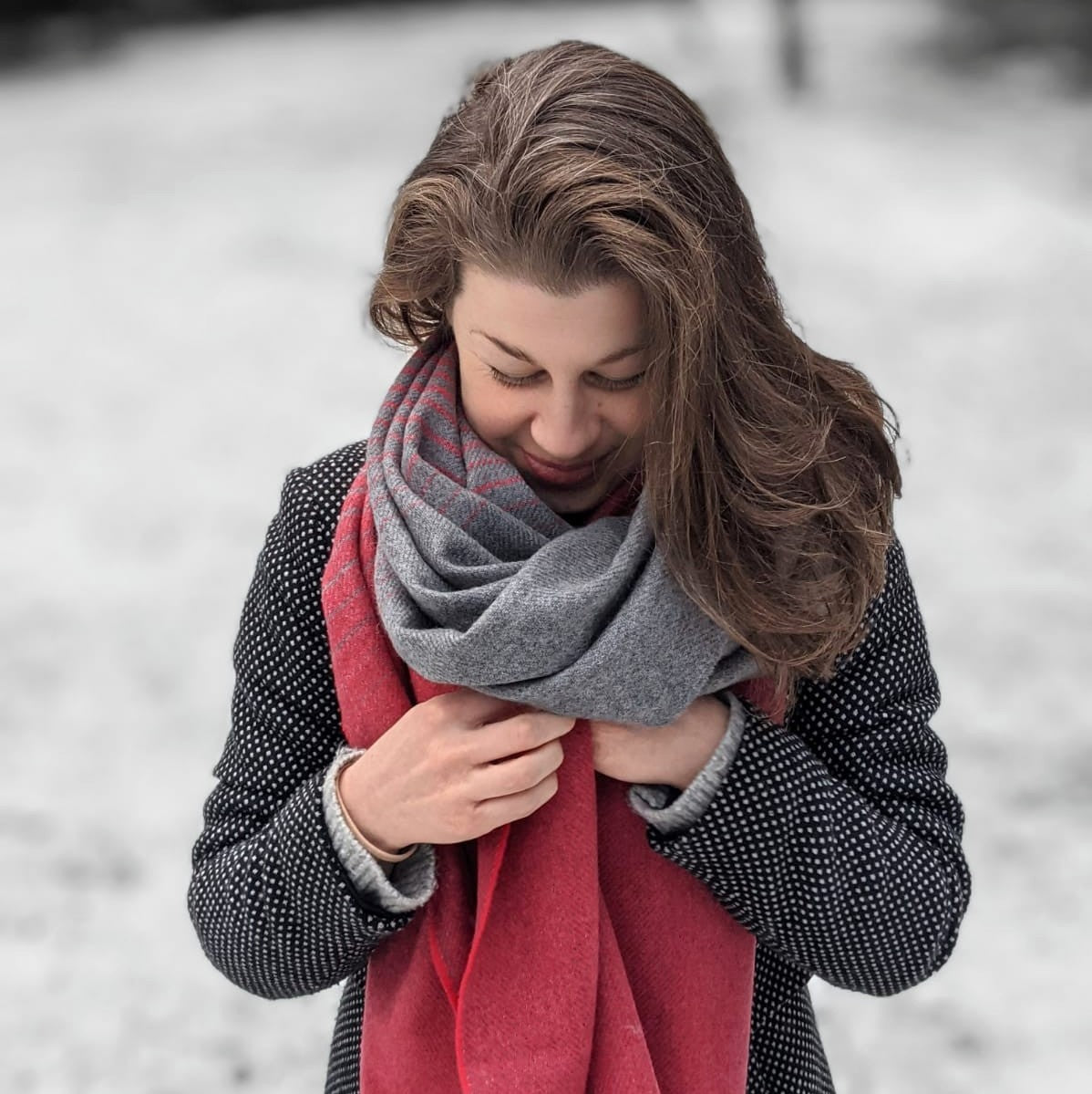 A woman with long hair, wearing a scarf and sweater, looks down, embodying winter fashion.