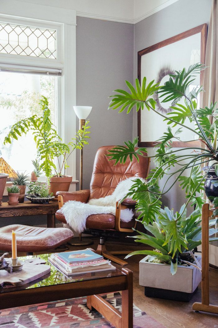 A brown leather chair with a white blanket beside a table holding potted plants and a stack of books in a cozy room.