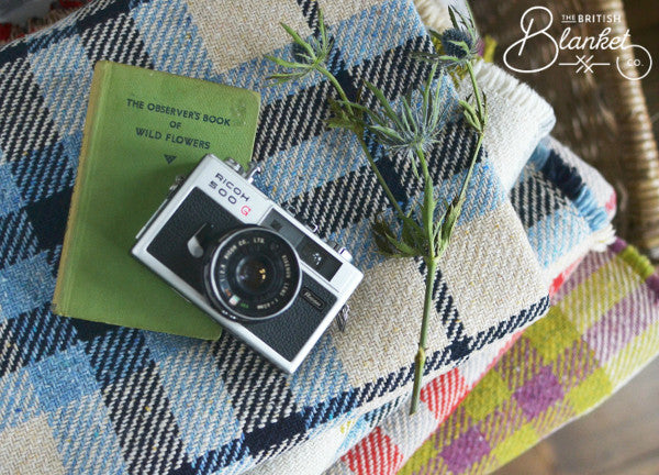 Close-up of a camera and a book resting on a blanket, highlighting the camera lens, suggesting a cozy indoor setting.