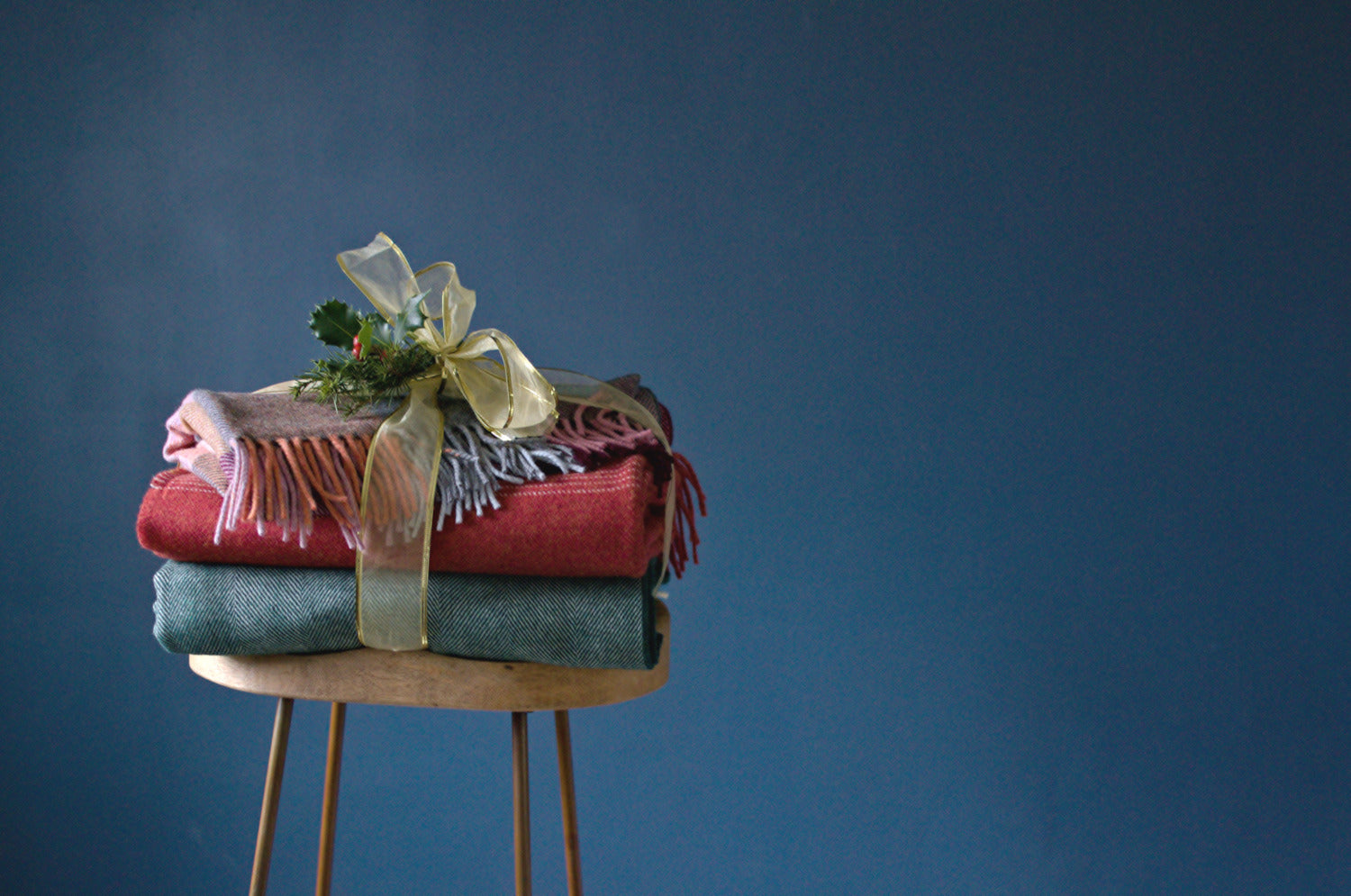 A stack of colorful blankets tied with a gold ribbon sits on a stool, showcasing their textures and colors prominently.
