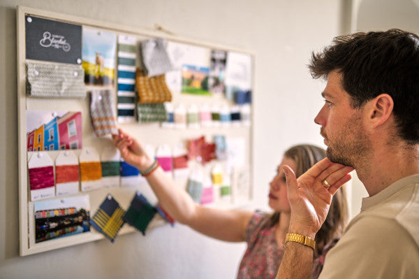 A man and woman examining fabric samples on a whiteboard; the woman points while the man contemplates with his hand on his chin.