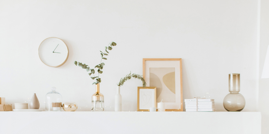 A shelf displays a picture frame, a gold vase with a branch, and a candle, with a wall clock seen above.