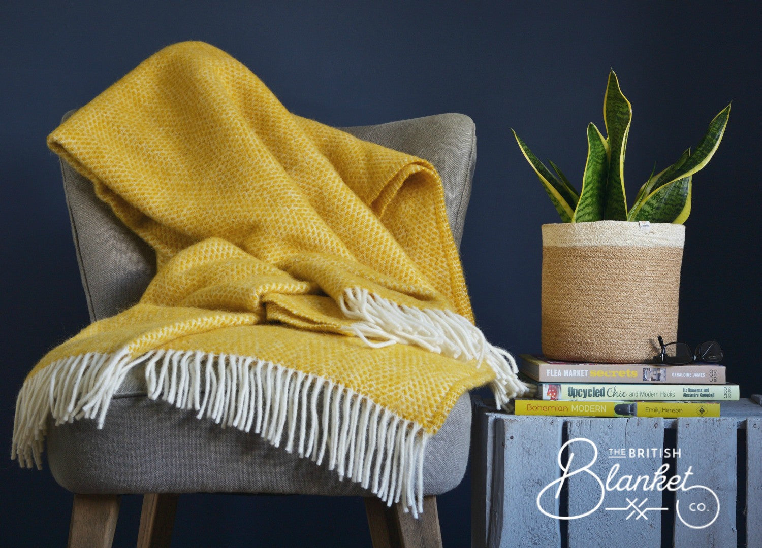 A yellow blanket draped over a chair beside a potted plant, set against a wooden fence, creating a cozy indoor setting.