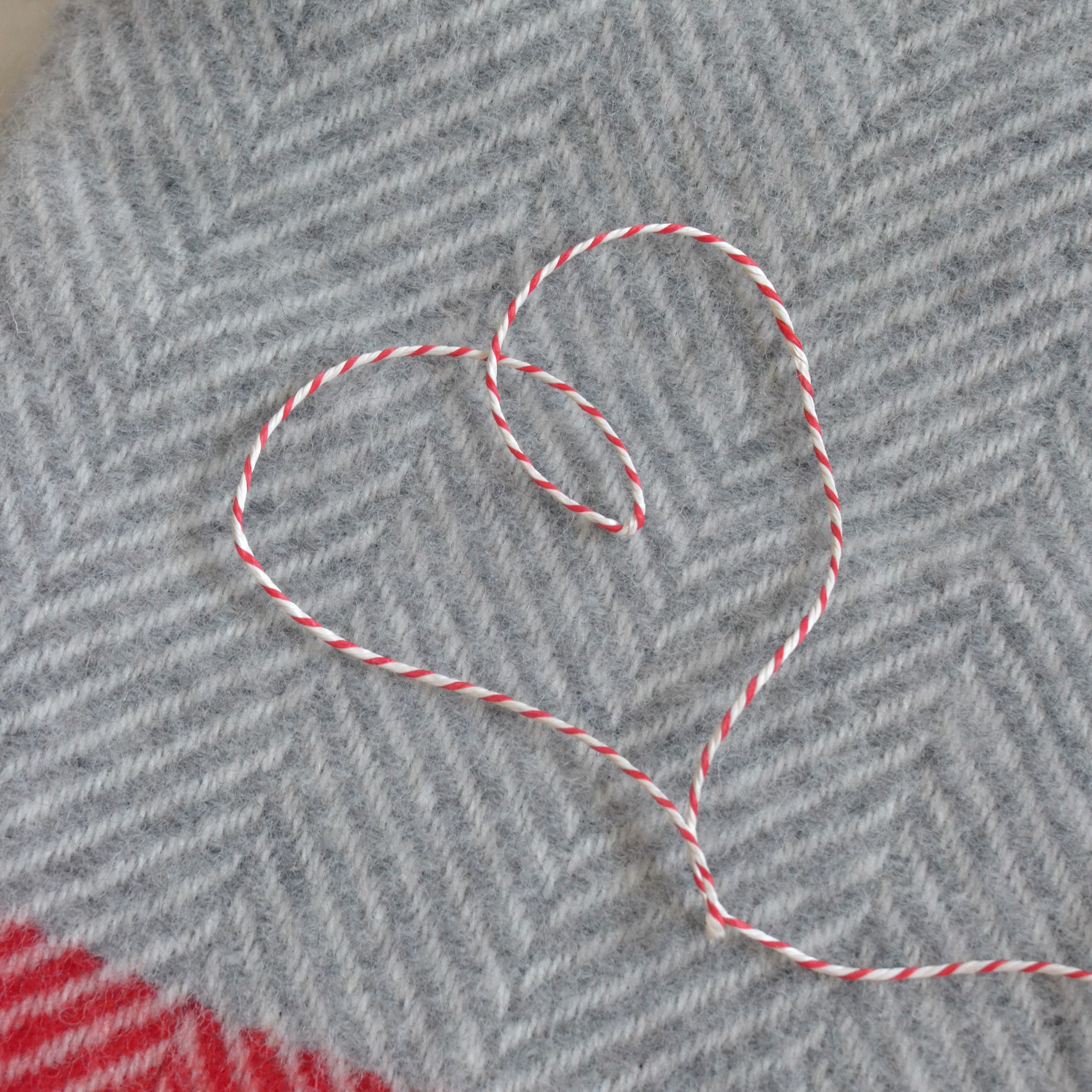 Heart-shaped red and white string on a textured gray and red blanket, showcasing intricate stitch and needlework patterns.