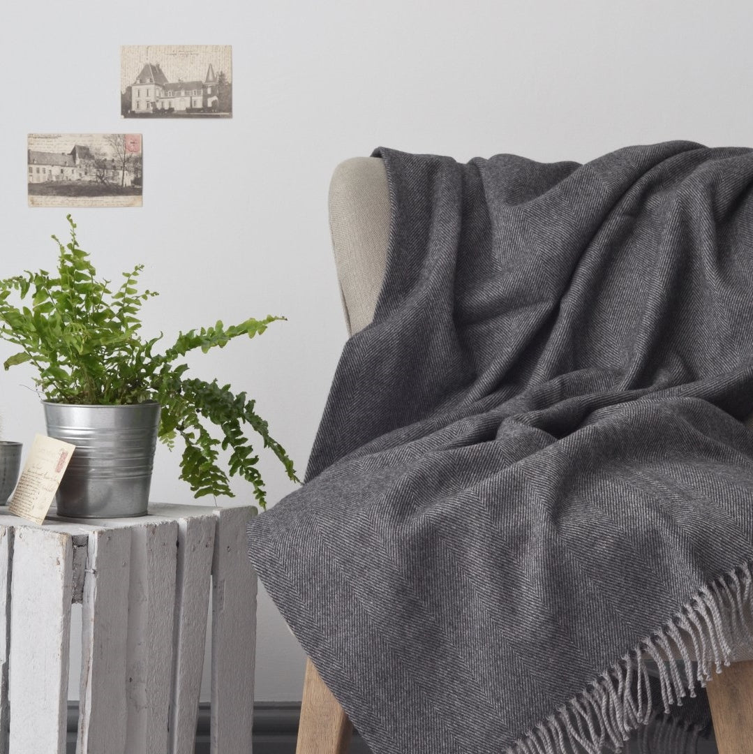 A grey blanket draped over a chair with a potted plant beside it, creating a cozy indoor setting.