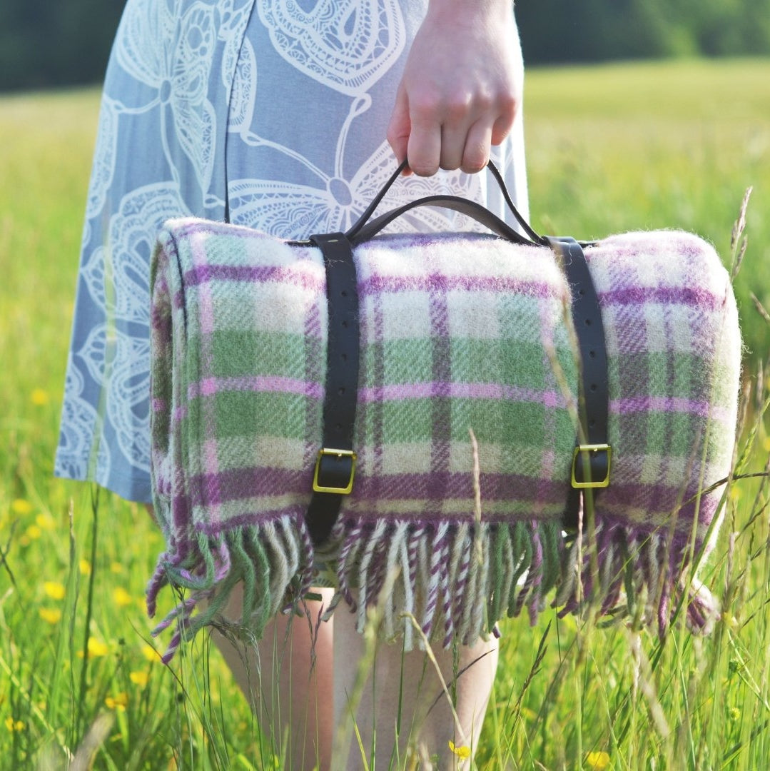 A person holding a blanket with straps in a grassy field, showcasing a close-up of the fabric and a black and yellow belt buckle.