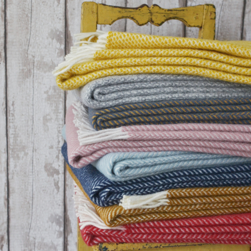 A stack of striped blankets on a chair, featuring various textiles with visible stitching and patterns, set against a white wood surface.