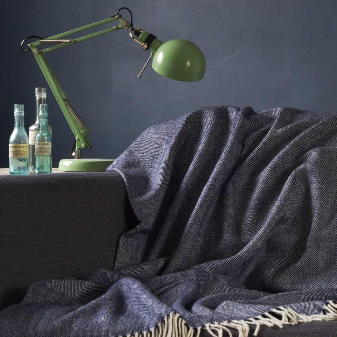 A green lamp and several bottles on a table, with a blanket draped over a nearby couch in an indoor setting.