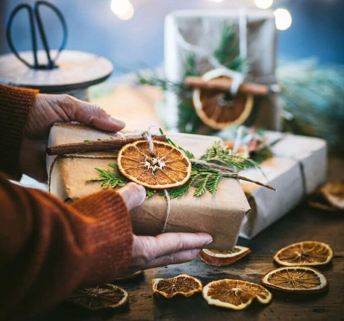 A person holding a wrapped present with visible slices of dried orange, set on a table, suggesting a festive or gift-giving scene.