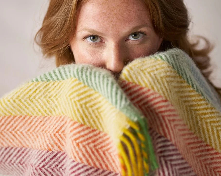 A woman partially covers her face with a striped blanket indoors, highlighting her eyes and the texture of the fabric.