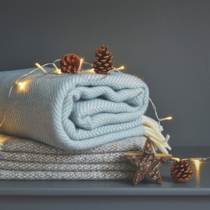 A stack of blankets adorned with string lights, featuring pine cones and a wooden star with white and blue yarn accents.