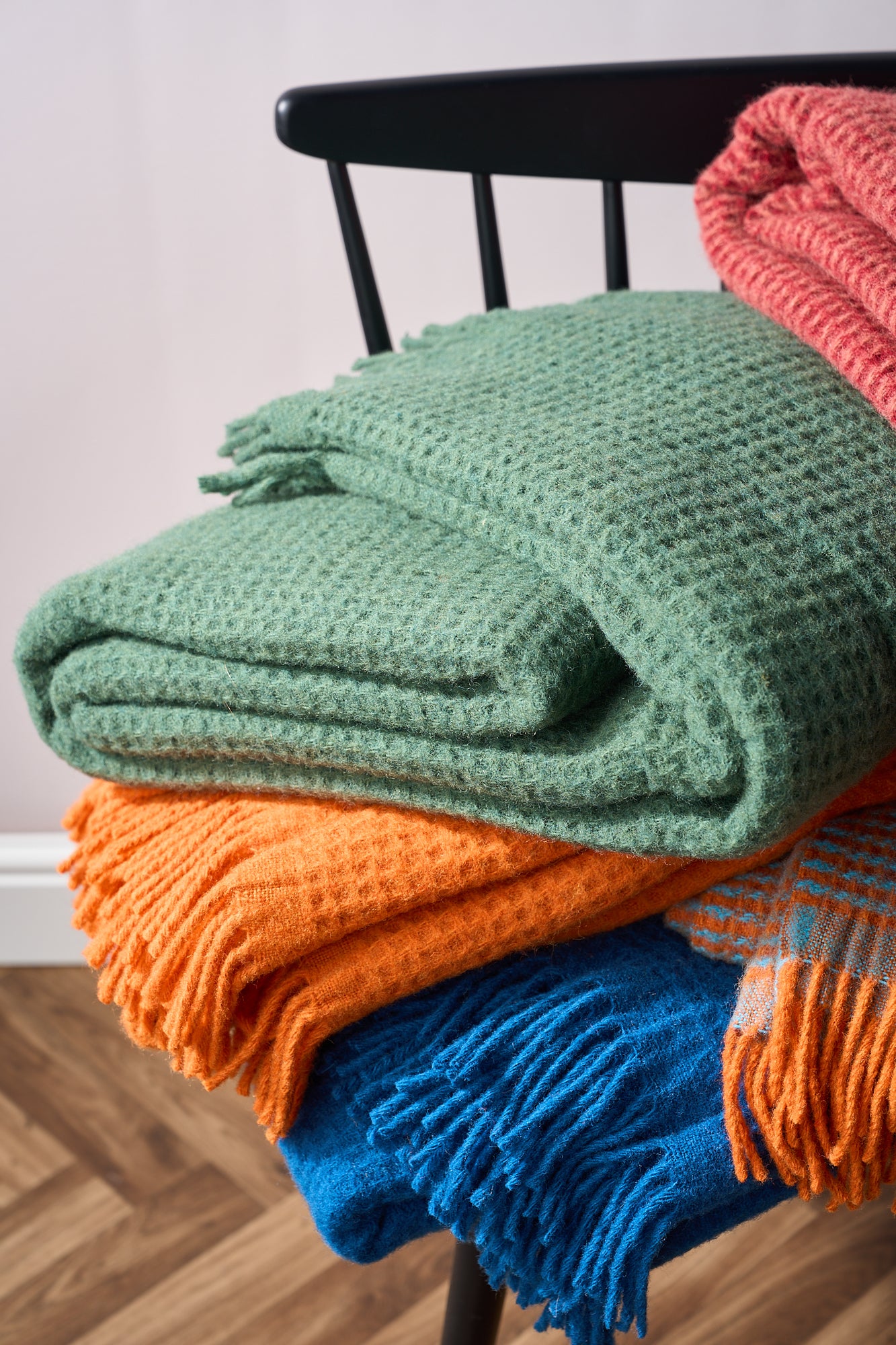 A stack of colorful knitted blankets neatly arranged on a wooden chair, showcasing various textures and patterns.
