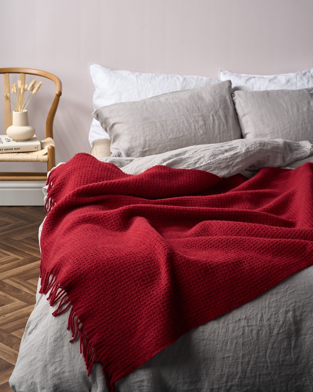 Red waffle wool blanket draped on a bed in a room with a styled chair and vase