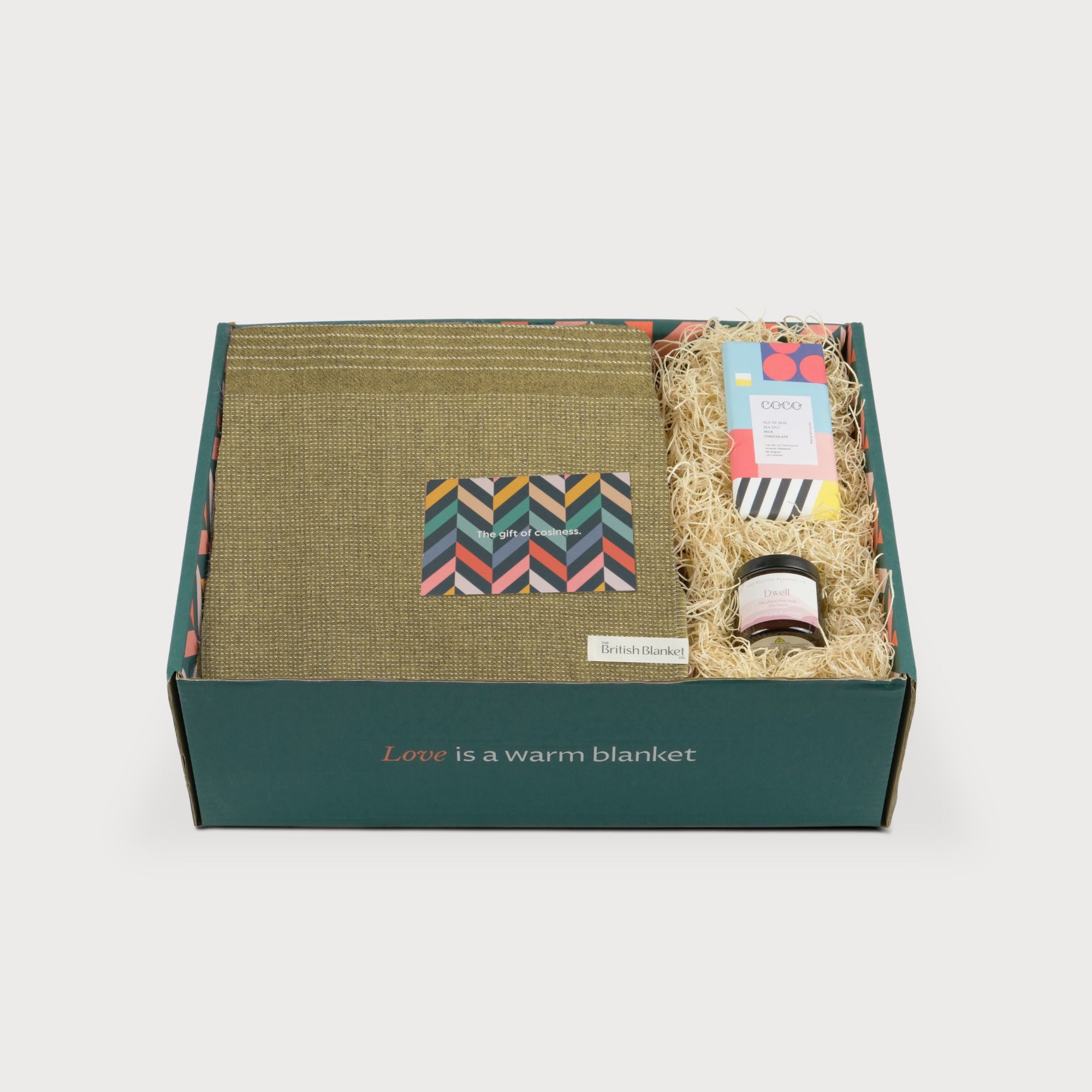 Alpaca Blanket Gift Box: Golden Moss includes an olive-green wool blanket, COCO chocolate, Dwell candle, and cozy-themed gift card in an eco-friendly dark green box.