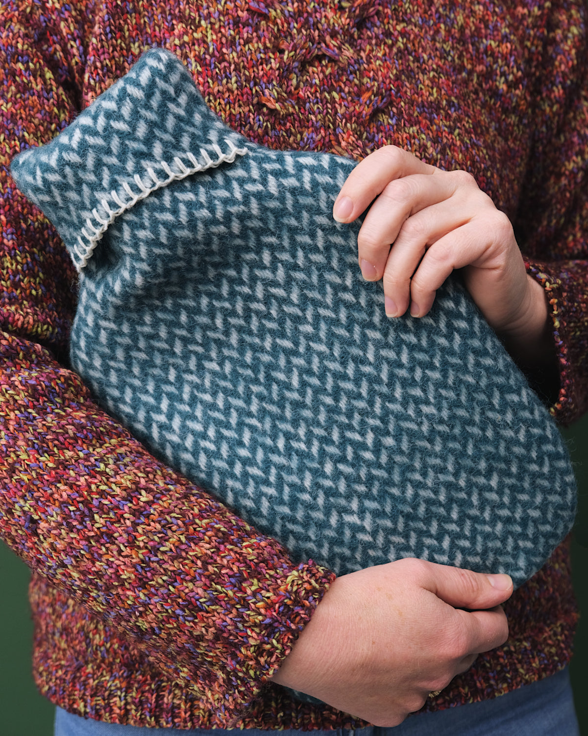 Person holding Hot Water Bottle with a knitted cover, designed for warmth. Part of a gift box for cozy nights.