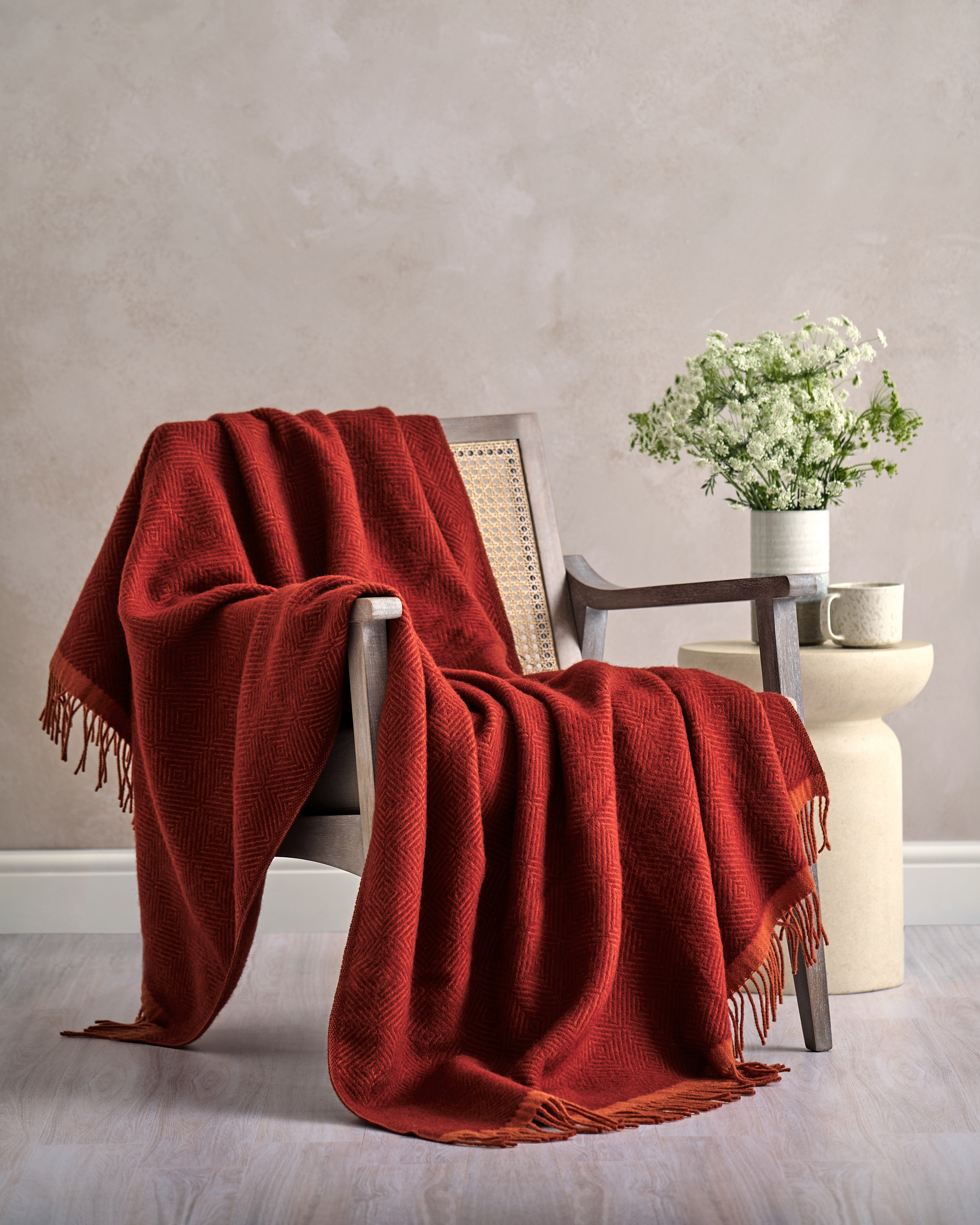 Wildweave Blanket Gift Box: Rowan & Beech, featuring a rust-red woven throw on a wooden chair, comes with a candle, chocolate, and gift box.