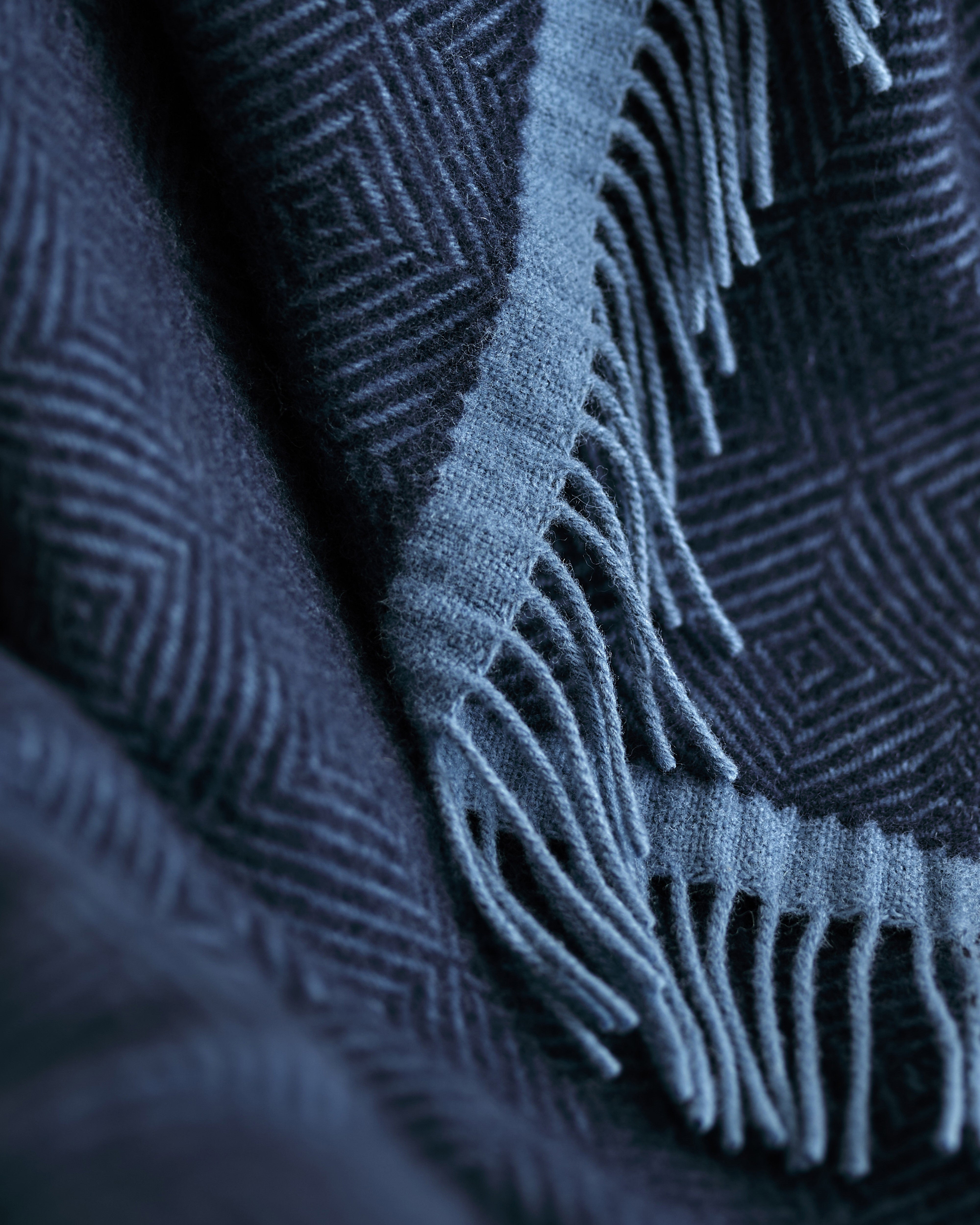 Wildweave Blanket Gift Box: Midnight & Dusk features a close-up of a wool blanket with blue geometric patterns and fringed edges, perfect for a cozy gift.