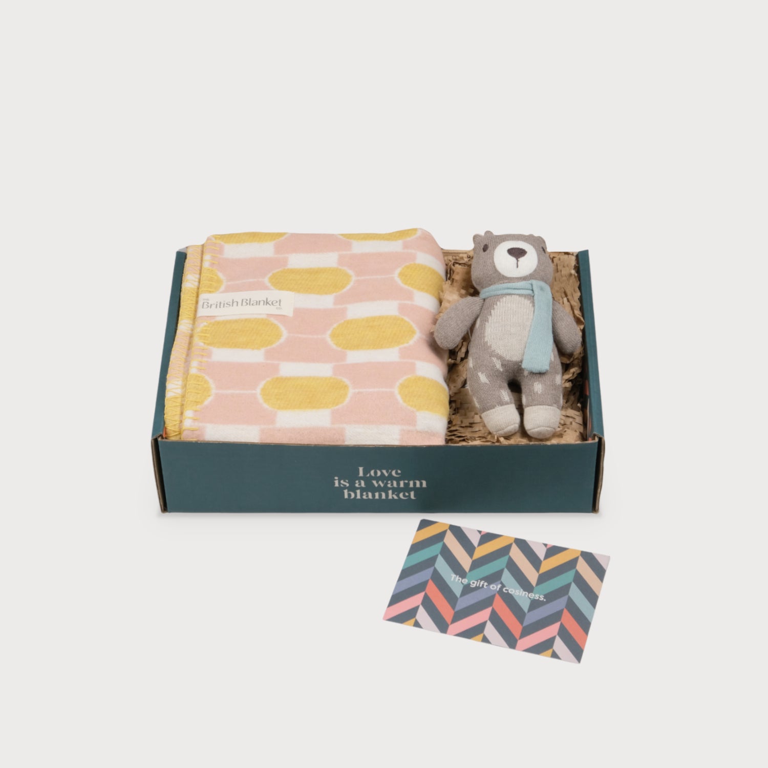 Cloud Cotton Baby Blanket Gift Box: Boatyard Glow with a pink-and-yellow geometric blanket, gray teddy bear with a blue scarf, and a chevron-patterned gift card.