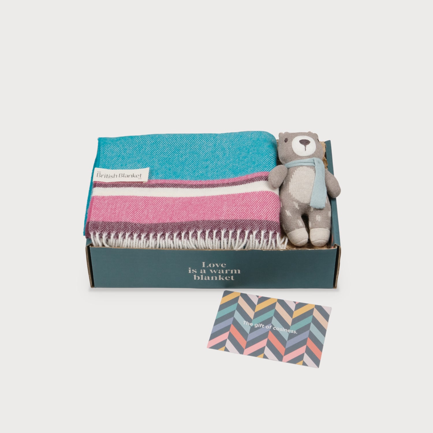 Merino Lambswool Baby Blanket Gift Box: Marina with a striped wool blanket, knitted teddy bear, and a The gift of cosiness card in an open box.