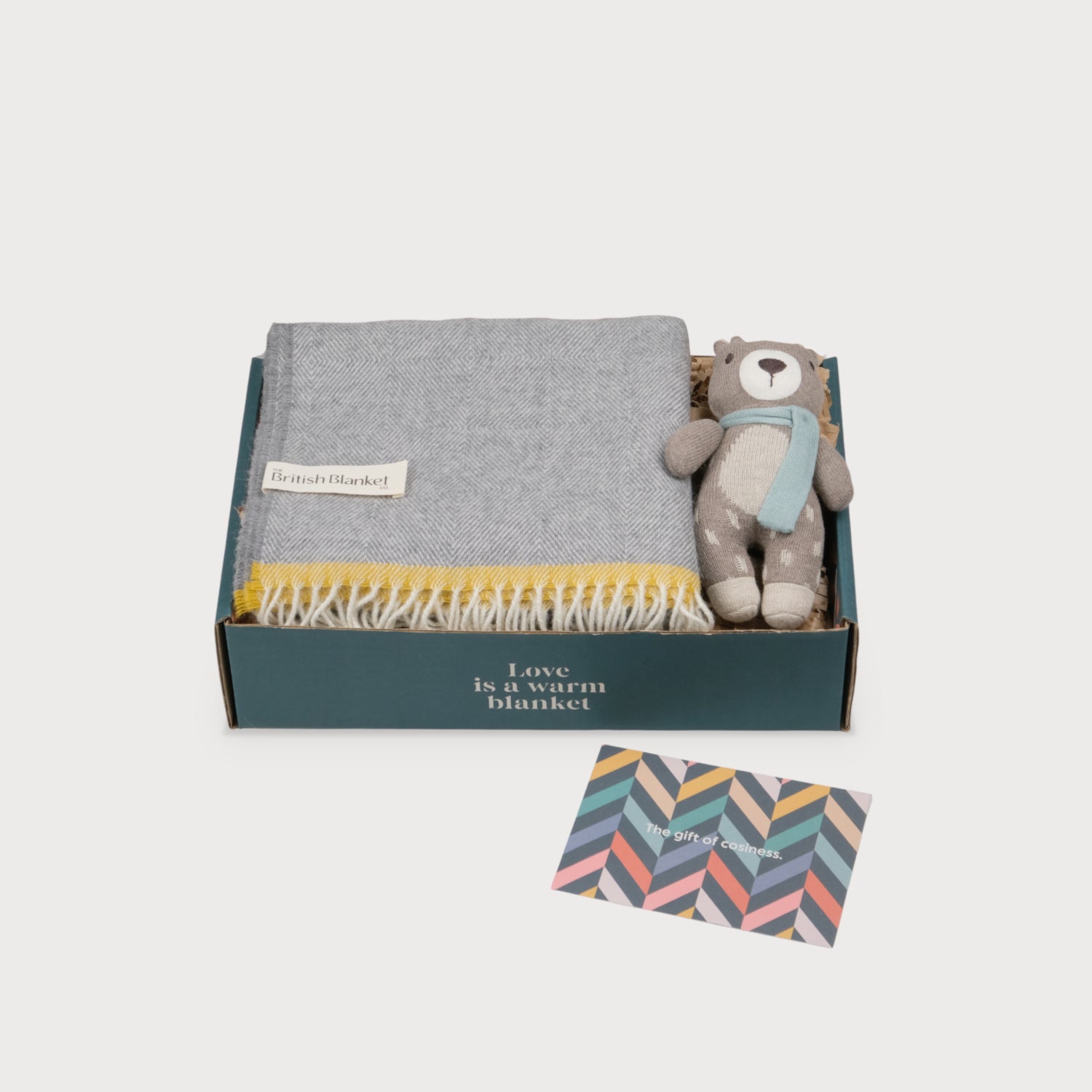 Merino Lambswool Baby Blanket Gift Box: Bumblebee features a grey herringbone wool blanket, knitted teddy bear with scarf, and a chevron-print card reading “The gift of cosiness.”