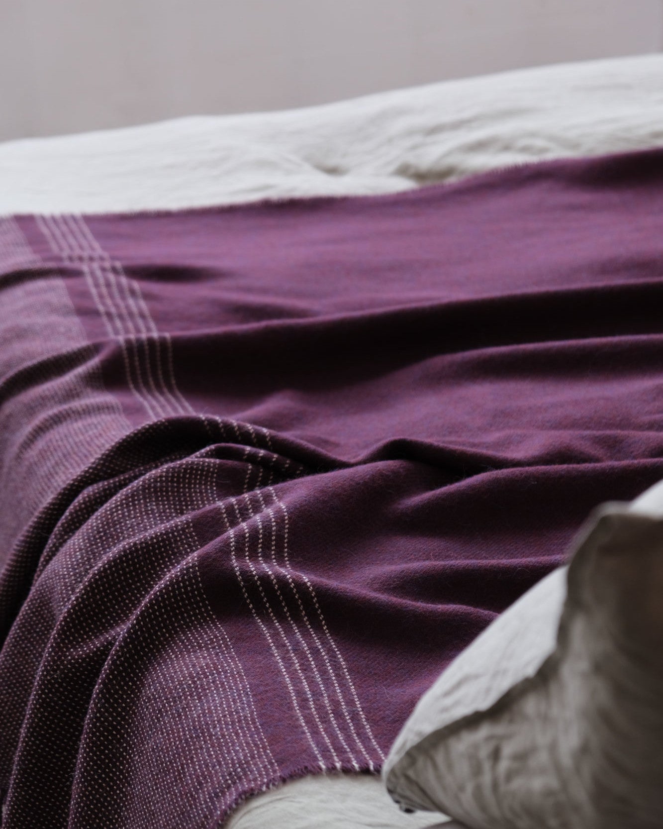 Alpaca Blanket Gift Box: Berry Purple, featuring a luxury alpaca blanket draped over a bed, with a matching pillow in view.