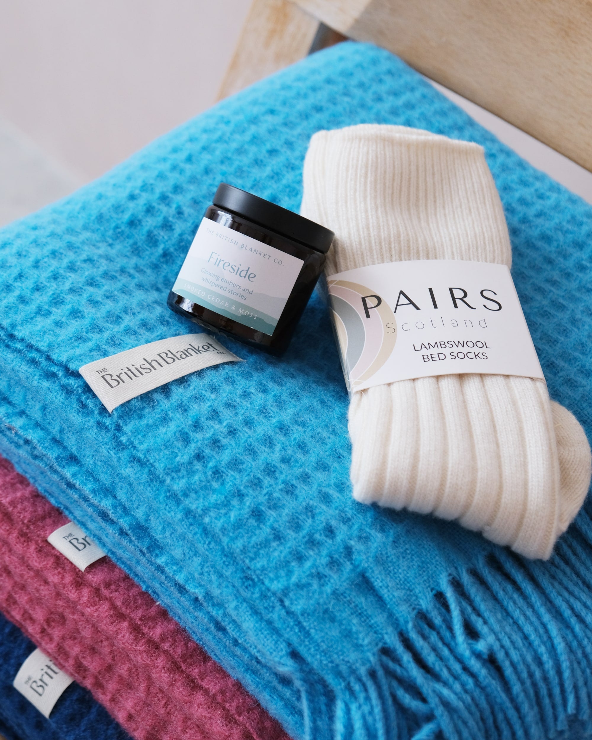 Bright Friday Blanket Bundle: Lido featuring a Totterdown Wool Waffle Blanket, lambswool bed socks, and a Fireside-scented amber candle on a wooden bench.