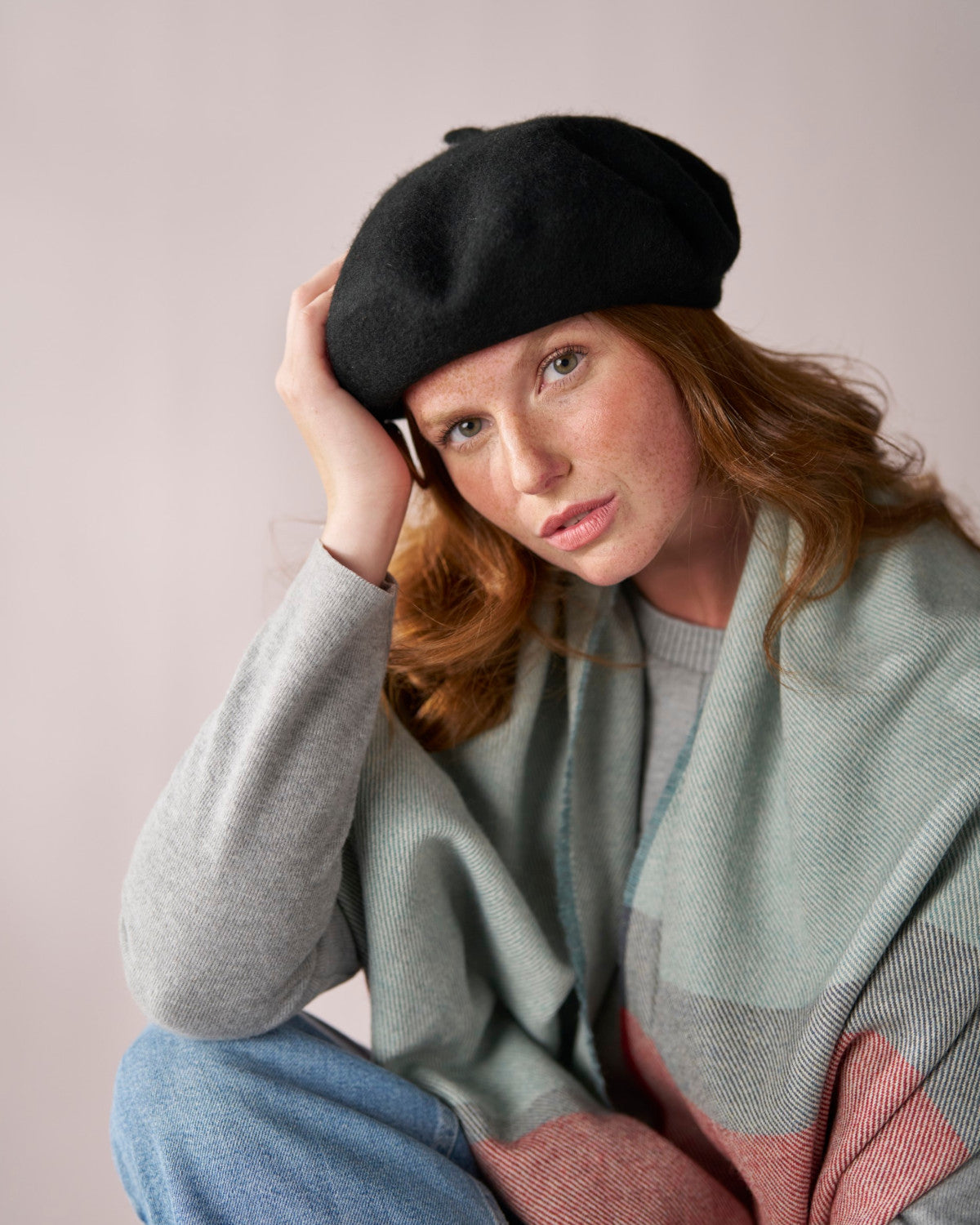 Young woman wearing a Wool Beret Hat: Black, featuring a tilted design, showcasing its thick felt quality and stylish pairing with a scarf and sweater.