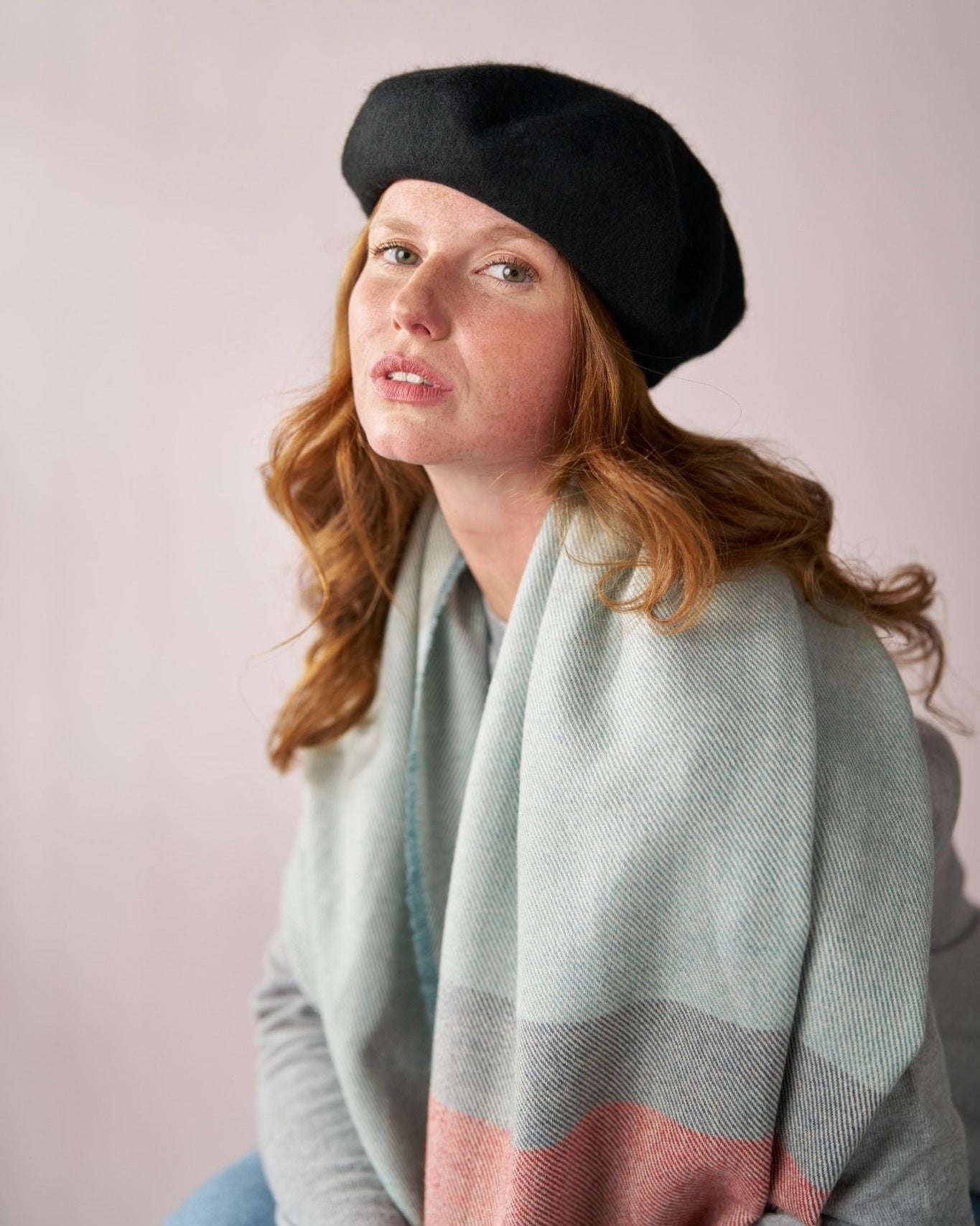 Young woman wearing a Wool Beret Hat: Black, showcasing its sleek shape and quality, paired with a woven scarf, highlighting the beret's versatile style.
