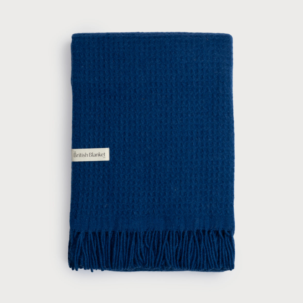 Bright Friday Blanket Bundle: Curious - a folded waffle-weave throw with fringe, featuring a “British Blanket” label on the edge.