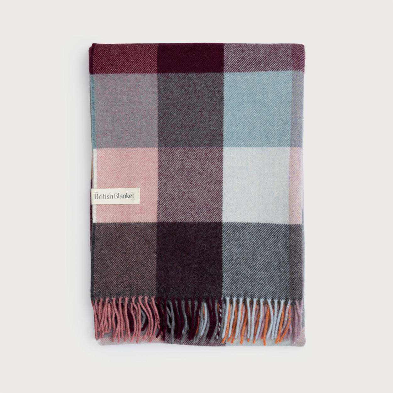 Merino Check Blanket: Burnished - A close-up of a fringed blanket with a checkered pattern, showcasing its fine merino lambswool weave and multicolored tassels.