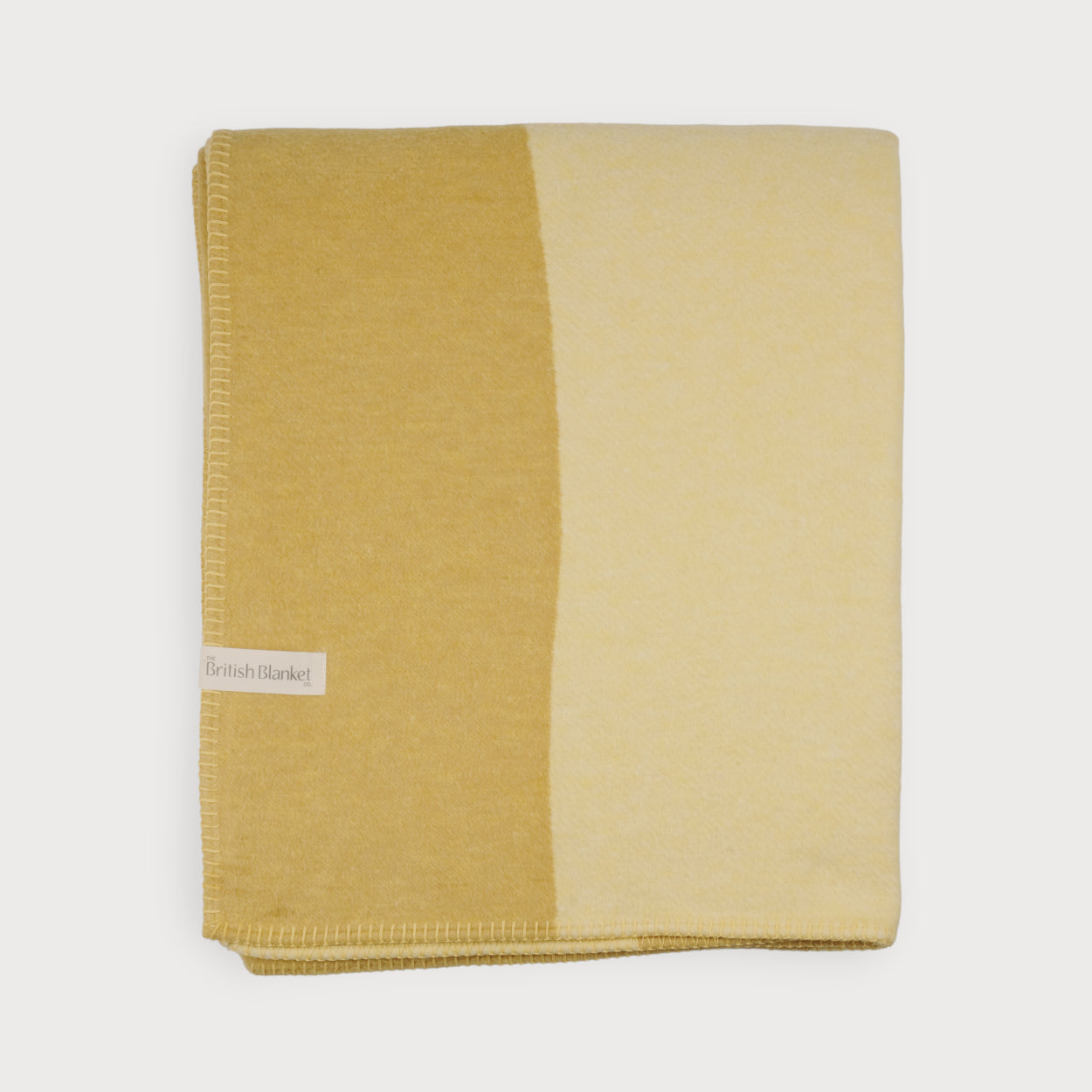 Cloud Cotton Blanket: Tide in Butter, featuring a two-tone yellow/cream color block design with a stitched edge and a small woven label reading “The British Blanket.”