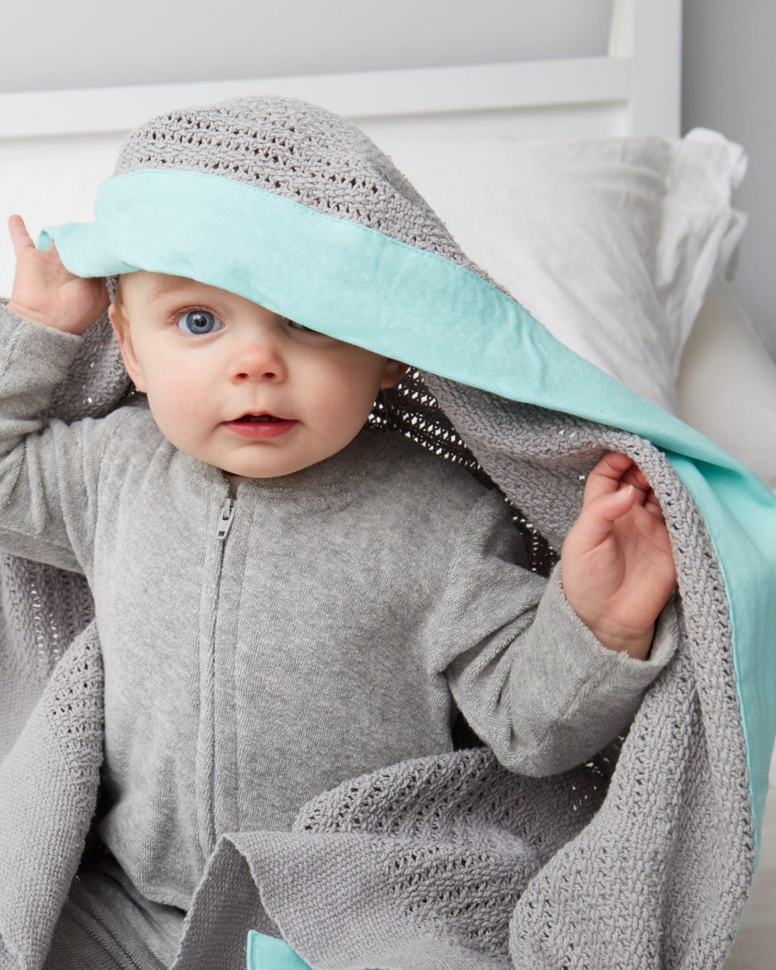 Baby wrapped in Organic Cotton Cellular Baby Blanket: Turquoise, wearing a grey outfit and bonnet, showcasing the blanket's breathable texture and premium quality.