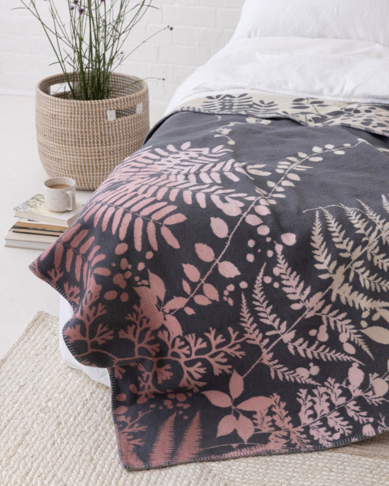 Clarissa Hulse Blanket: Kaleidoscope in Shell, draped on a bed with a fern pattern in pink and cream, adds a cozy touch to a minimalist bedroom scene.