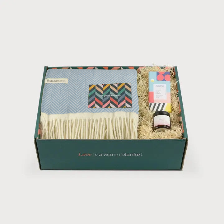 Clifton Blanket Hamper: Harbourside includes a herringbone-patterned throw, geometric tea box, colorful card, and a small jar in a dark green gift box.