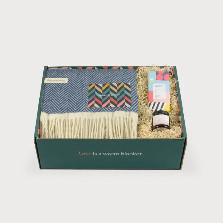 Clifton Blanket Hamper: Steamship featuring a herringbone wool blanket, colorful card, bath bar, and jar in a dark green box with “Love is a warm blanket.”