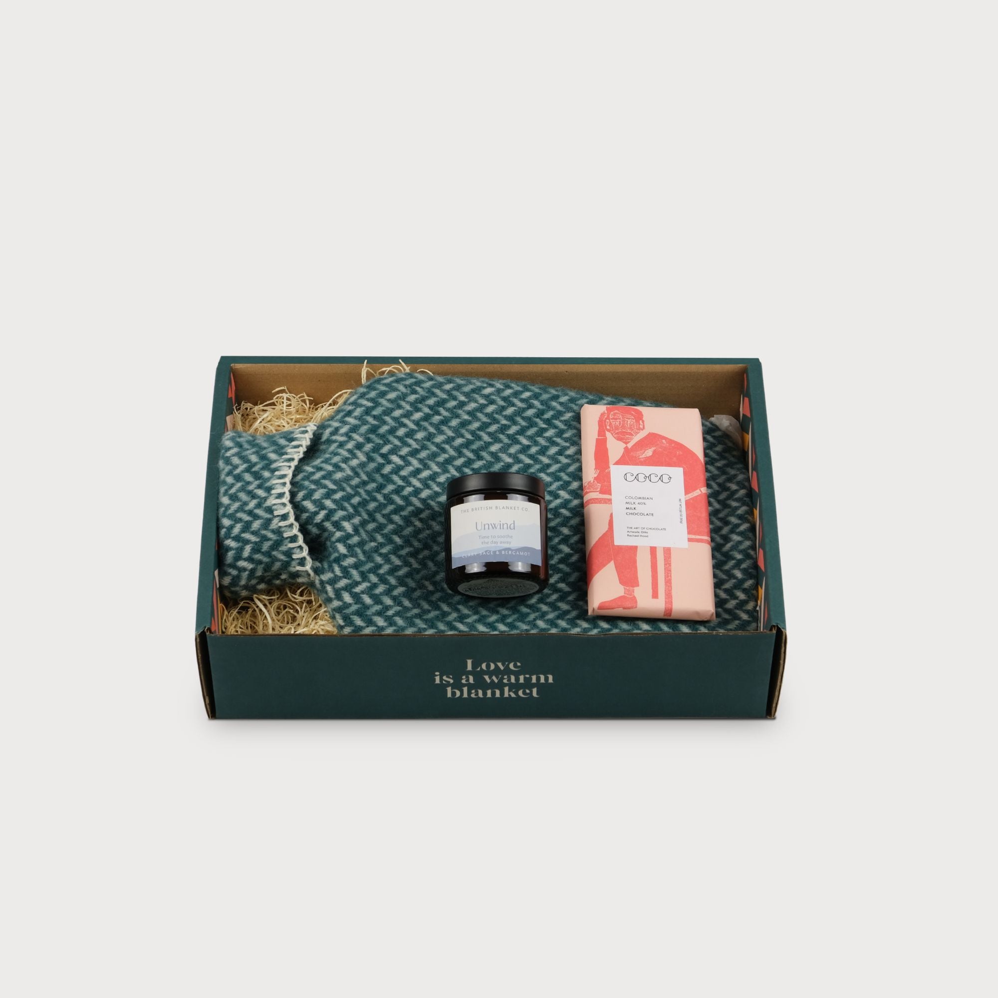 Cosy Gift Box: Self-Love featuring a blue and white blanket, nestled among wood shavings, with a visible product description on white paper.