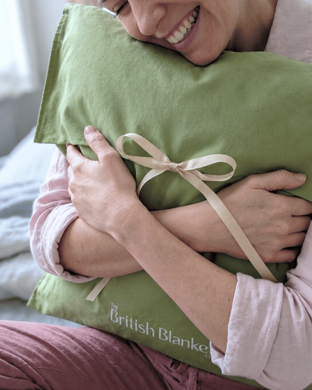 Woman hugs a green cotton gift bag for a blanket tied with a cream ribbon and The British Blanket Co logo on the frong