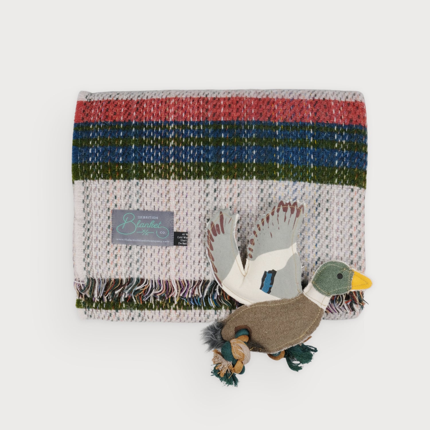 Cosy Gift Set: Dog Blanket & Toy features a fringed wool blend throw with stripes, paired with a duck-shaped dog toy draped across the edge.