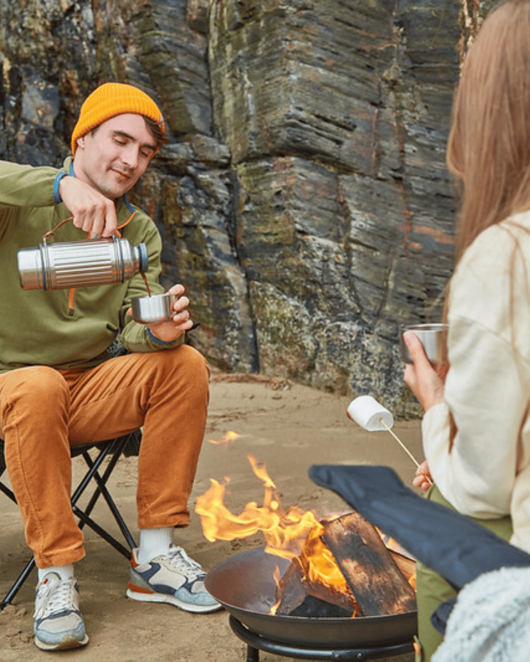 Couple roasting marshmallows on the beach while having a drink with Black + Blum Flask